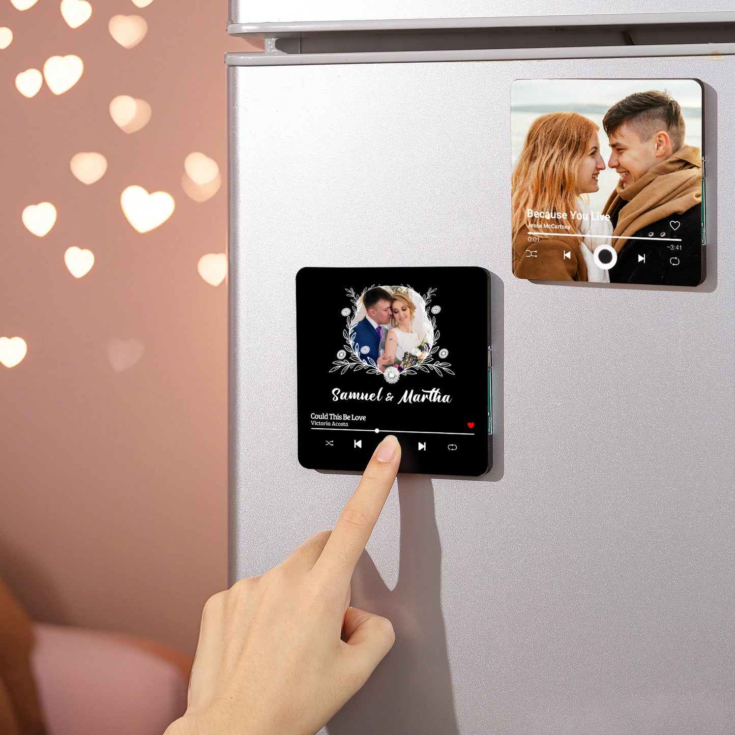 Two personalized song magnets on a refrigerator, with a hand pressing the play button on the first magnet.