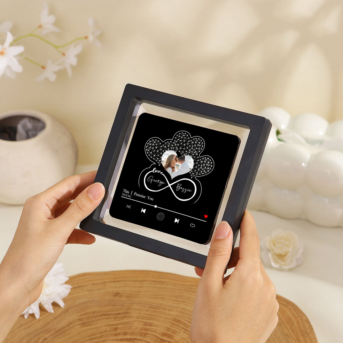 Hands holding a black framed music plaque with hearts and an image of a couple.
