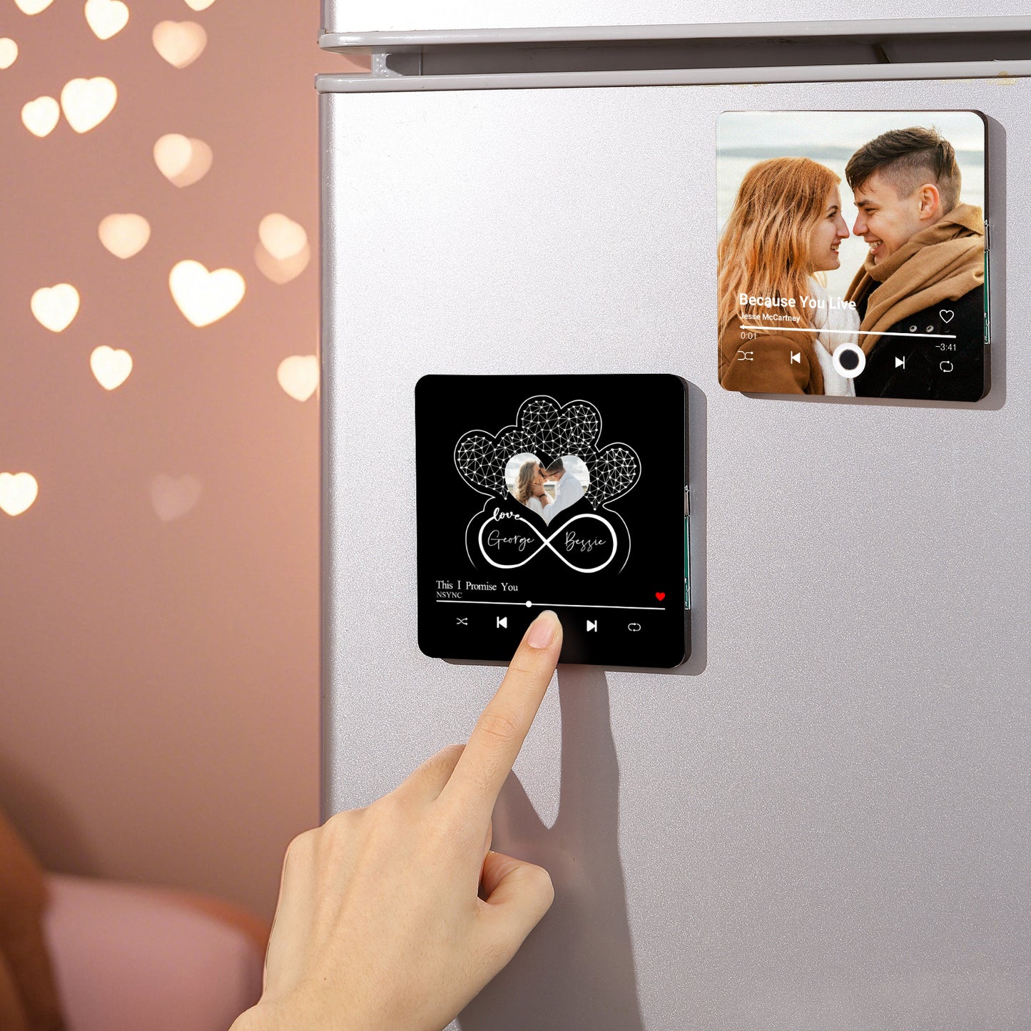 Close-up shot of two personalized magnets on a refrigerator: one displaying a couple looking at each other with a song title, "Because You Live" by Jesse McCartney, and the other with a couple inside a heart-shaped design with names and the song "This I Promise You" by NSYNC.