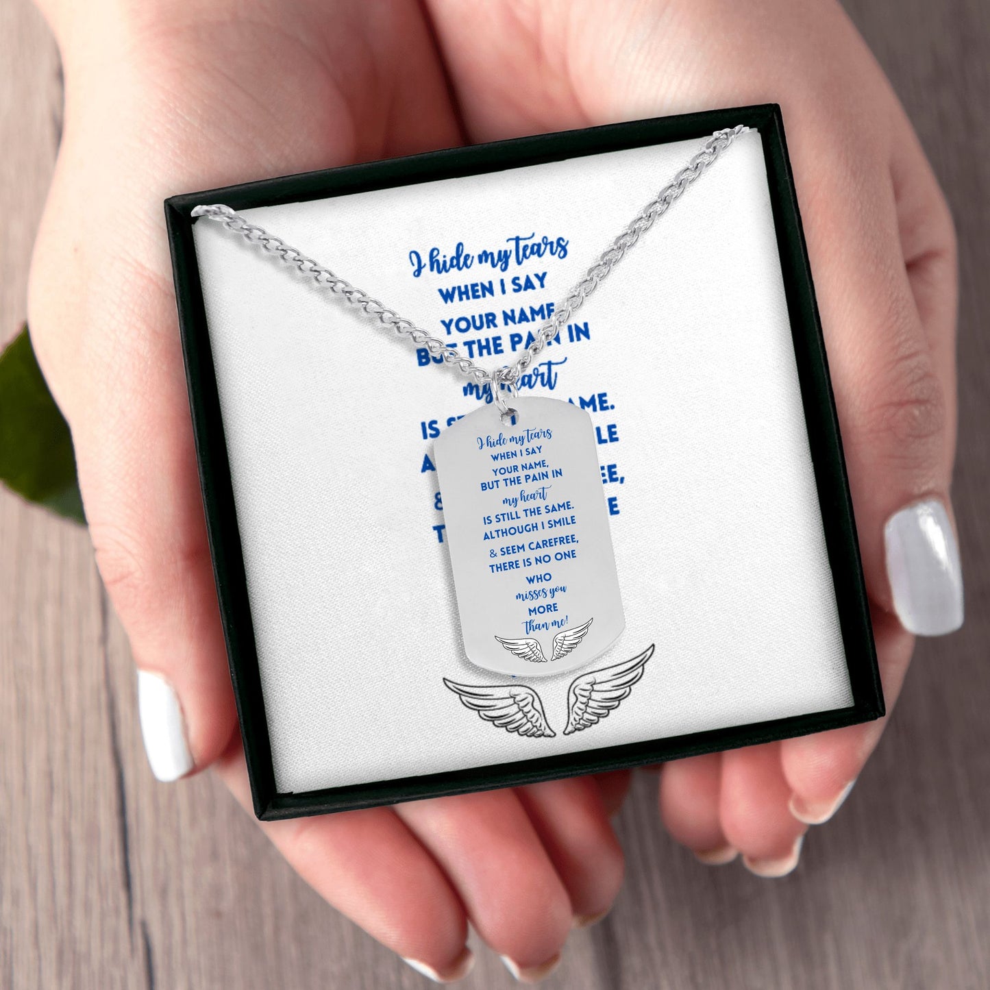Silver steel memorial dog tag necklace with engraved blue text and angel wings on white background in black gift box held in .