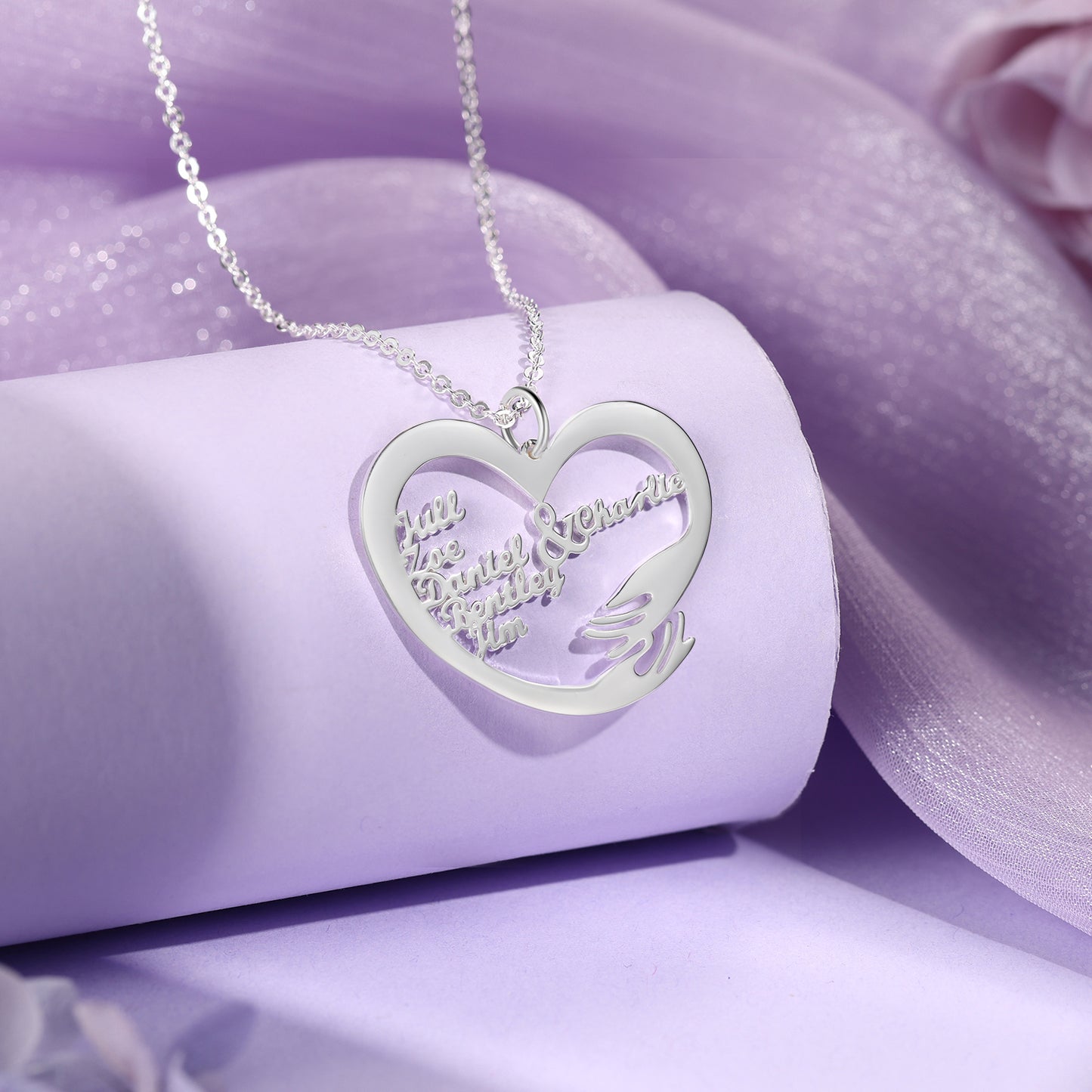 Silver heart-shaped pendant necklace with two names inside and a small hugging hand detail.