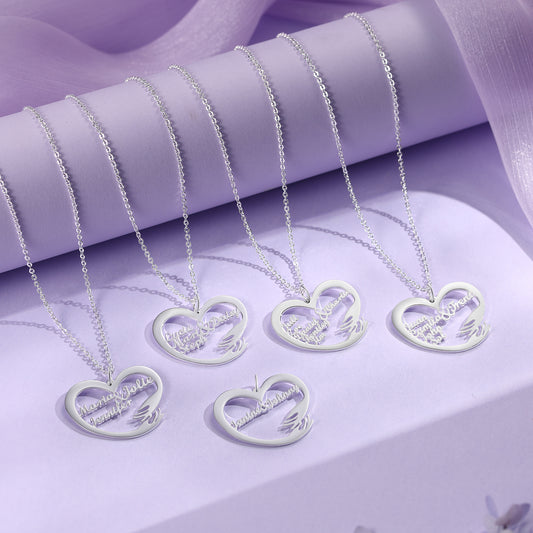 Five white gold plated heart-shaped name necklaces with delicate chains displayed on lavender fabric and jewelry holder.