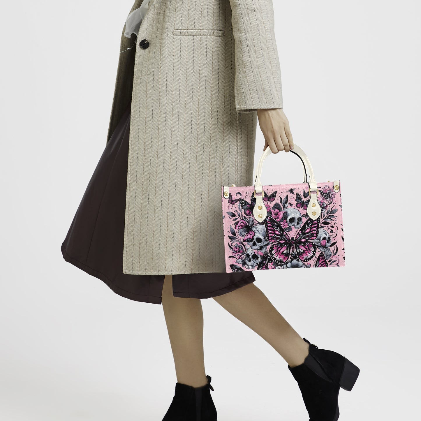 Person holding a pink handbag with floral and skull design against a white background