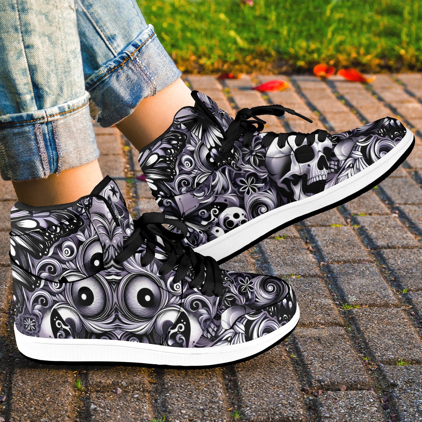High-top sneakers with black and white skull and eye design worn on a paved surface.