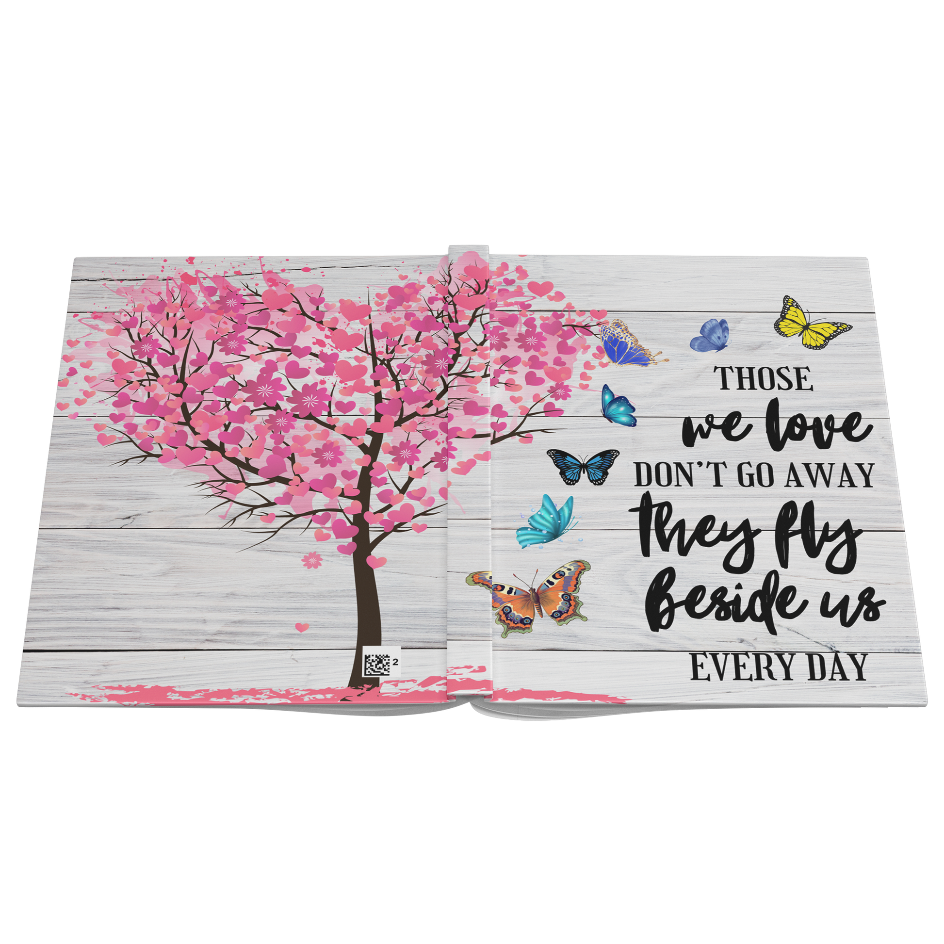 Open memorial journal with pink cherry blossom tree shaped as a heart and colorful butterflies on rustic white wood.